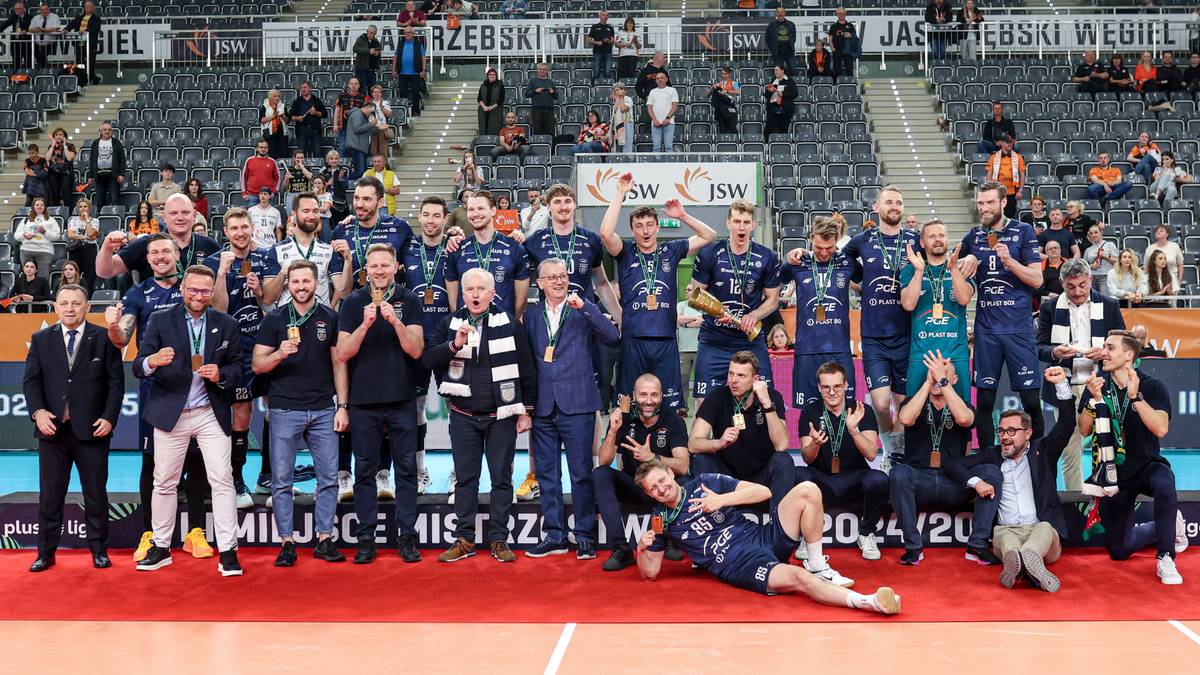 Drużyna siatkarzy Projektu Warszawa na czerwonym dywanie, trzymająca medal i puchar. Widoczni są gracze, sztab szkoleniowy i zarząd klubu. Na drugim planie trybuny wypełnione kibicami.