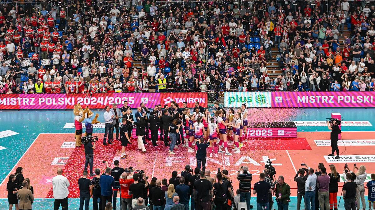 Piłkarki siatkowe świętują zwycięstwo na boisku, otoczone przez kibiców na trybunach.