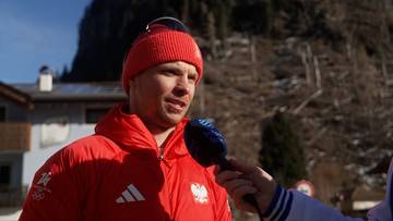 Maciej Staręga, polski skoczek narciarski w czerwonej kurtce i czapce, udziela wywiadu trzymając mikrofon.