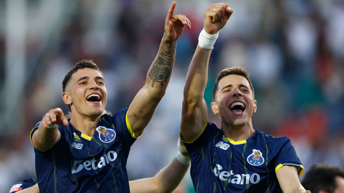 Dw&oacute;ch piłkarzy w niebieskich koszulkach FC Porto świętuje zwycięstwo, unosząc ręce w g&oacute;rę i uśmiechając się radośnie.