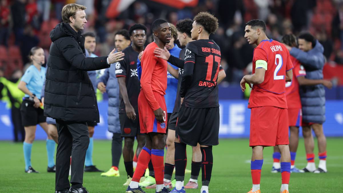 Trener piłkarski rozmawia z zawodnikami w czerwonych i czarnych strojach na boisku.