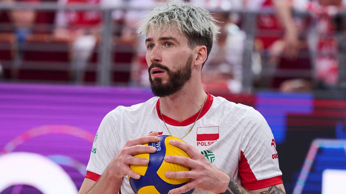 Mężczyzna w koszulce z orzełkiem reprezentacji Polski trzyma piłkę do siatkówki, zamyślony.
