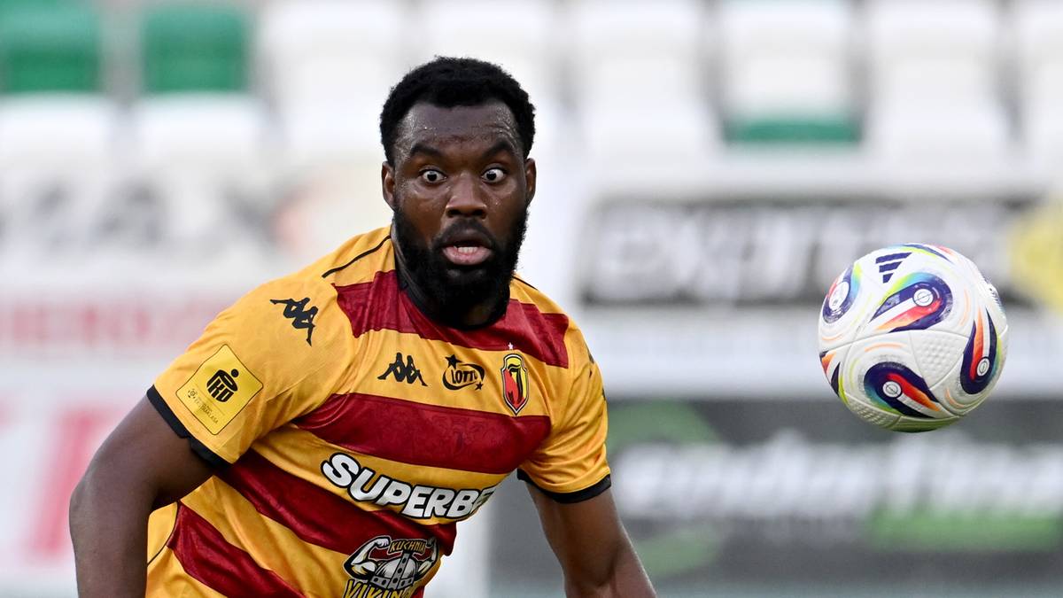 Piłkarz Jagiellonii Białystok w żółto-czerwonej koszulce z czarnymi pasami, biegnie w kierunku piłki.