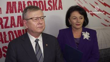 Mężczyzna w okularach i garniturze oraz kobieta w fioletowym kostiumie stoją obok siebie.