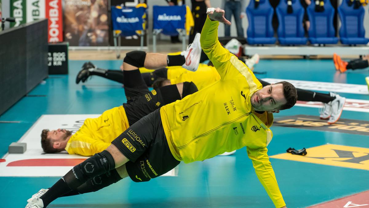 Siatkarz w żółtej koszulce wykonuje ćwiczenie rozciągające na macie.