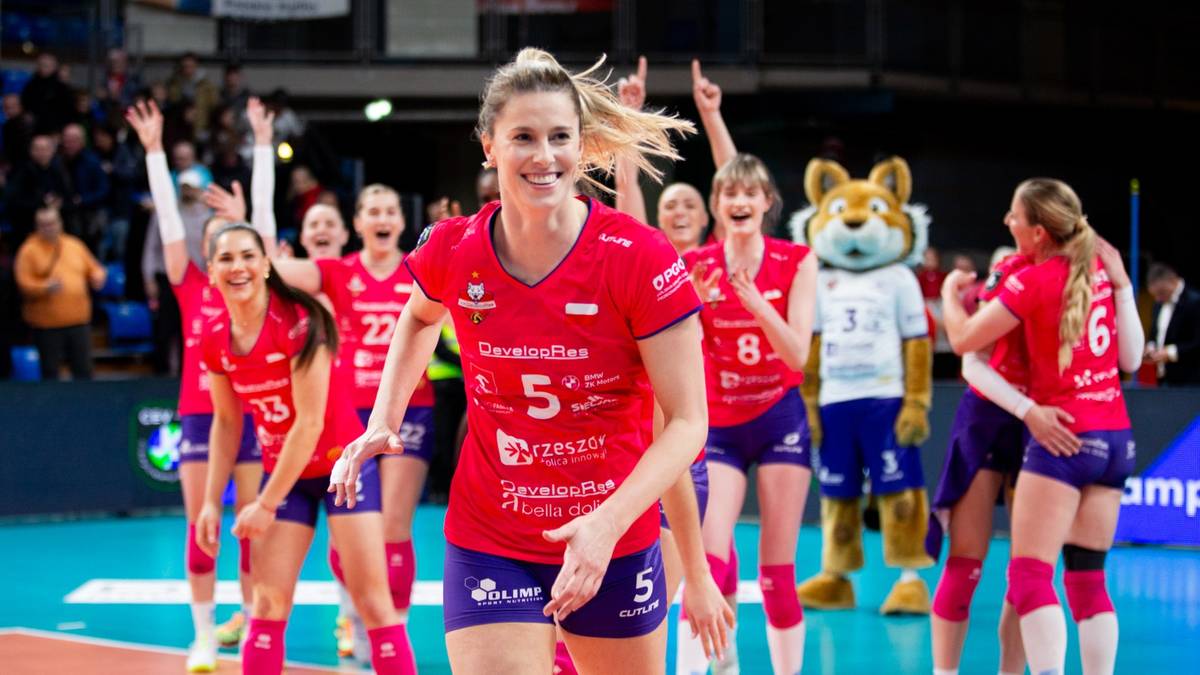 Grupa siatkarek w czerwonych strojach sportowych świętuje zwycięstwo na boisku. W centrum uśmiechnięta zawodniczka z numerem 5.