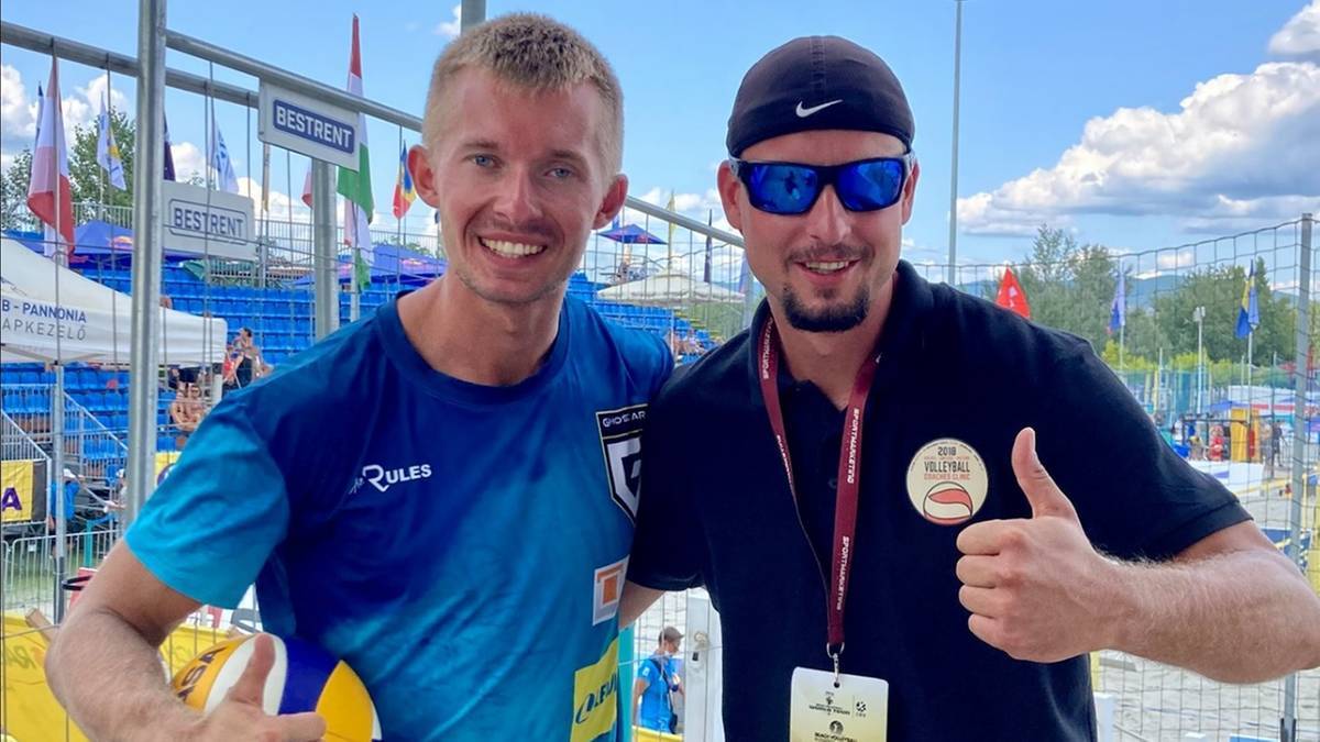 Dw&oacute;ch mężczyzn w strojach sportowych pozuje do zdjęcia, jeden z nich trzyma piłkę do siatk&oacute;wki.