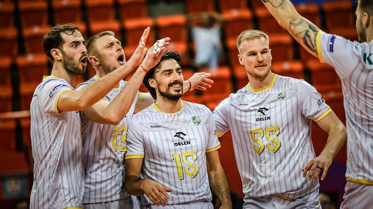 Grupa siatkarzy w biało-ż&oacute;łtych strojach świętuje zwycięstwo, jeden z zawodnik&oacute;w unosi rękę w geście triumfu.