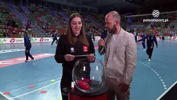 Kobieta i mężczyzna uczestniczą w losowaniu p&oacute;łfinał&oacute;w Pucharu Polski. W tle widać halę sportową z zawodnikami i widzami.