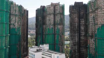 Widok z góry na zniszczone po pożarze wieżowce w Hongkongu, niektóre z nich pokryte zielonymi siatkami ochronnymi.