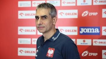 Trener reprezentacji Polski w piłce ręcznej, Jota Gonzalez, stoi przed ścianą z logo sponsor&oacute;w.