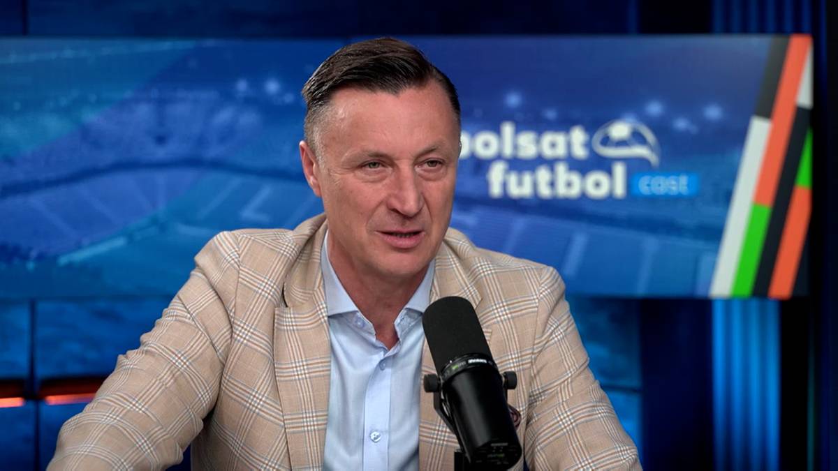 Mężczyzna w beżowej marynarce siedzi przed mikrofonem na tle ekranu z logo "Polsat Futbol Cast".