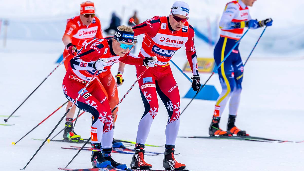 Narciarze biegowi w czerwono-białych strojach na ośnieżonym stoku, z kijkami i nartami.