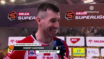 Robert Kamyszek, siatkarz w czerwonej koszulce, uśmiecha się podczas wywiadu na tle baner&oacute;w "ORLEN SUPERLIGA".