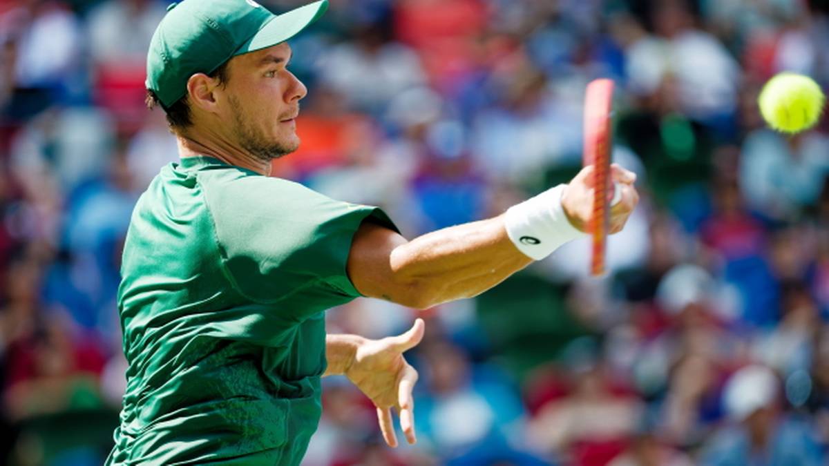 Hubert Majchrzak w trakcie meczu tenisowego, w zielonej koszulce i czapce, odbija piłkę rakietą.