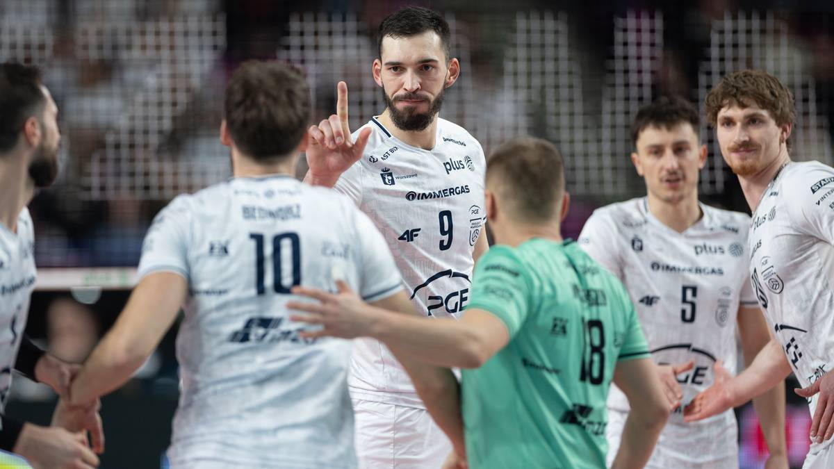 Siatkarze PGE Projekt Warszawa w białych strojach podczas meczu, jeden z zawodnik&oacute;w pokazuje palcem w g&oacute;rę.