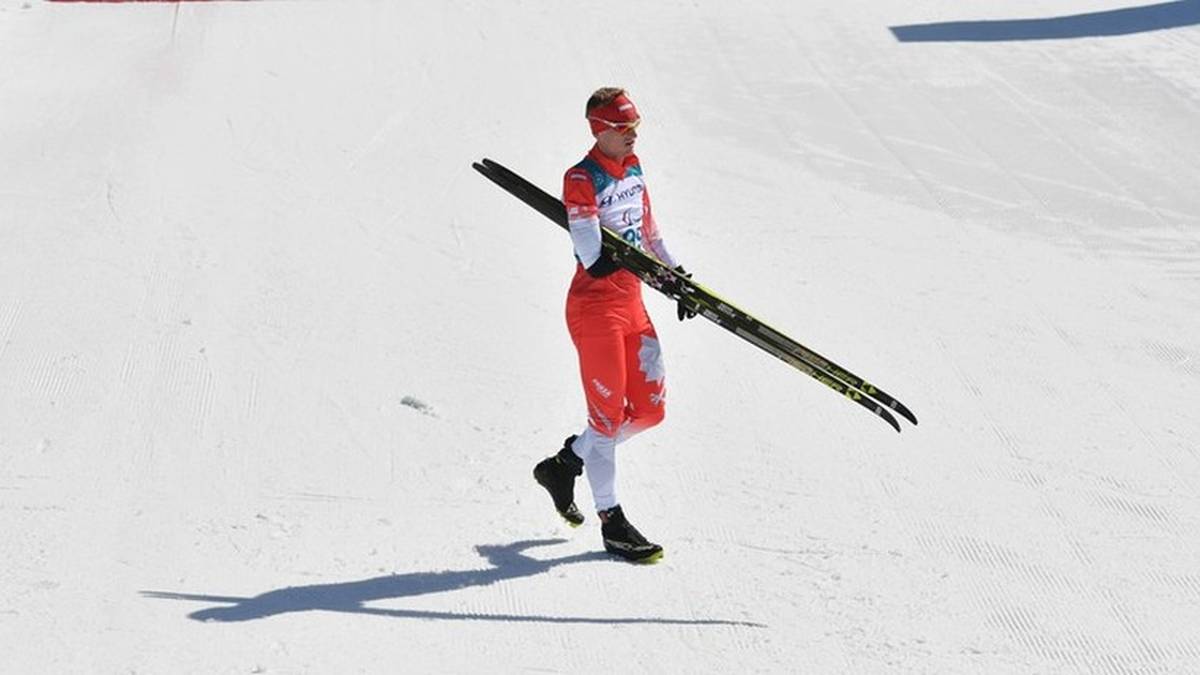 Narciarz w czerwonym stroju sportowym trzymający narty na ośnieżonym stoku.