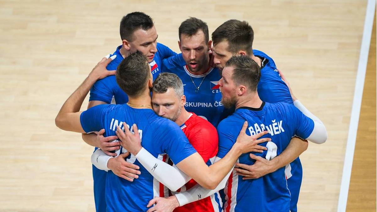 Sześciu siatkarzy w niebieskich strojach ściska się w okręgu, patrząc na siebie z determinacją. W środku jeden z zawodników ma czerwony strój.