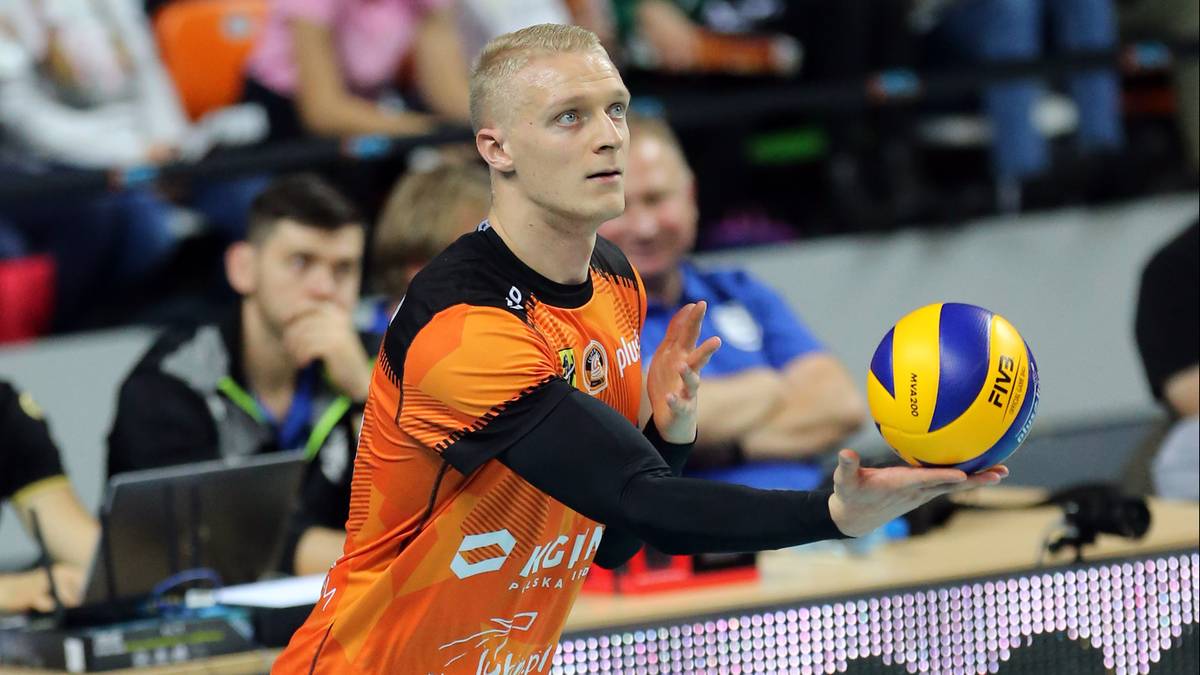 Siatkarz w pomarańczowej koszulce z numerem 23 na plecach serwuje piłkę.