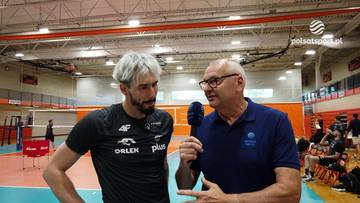 Siatkarz i dziennikarz rozmawiają w hali sportowej, trzymając mikrofon.