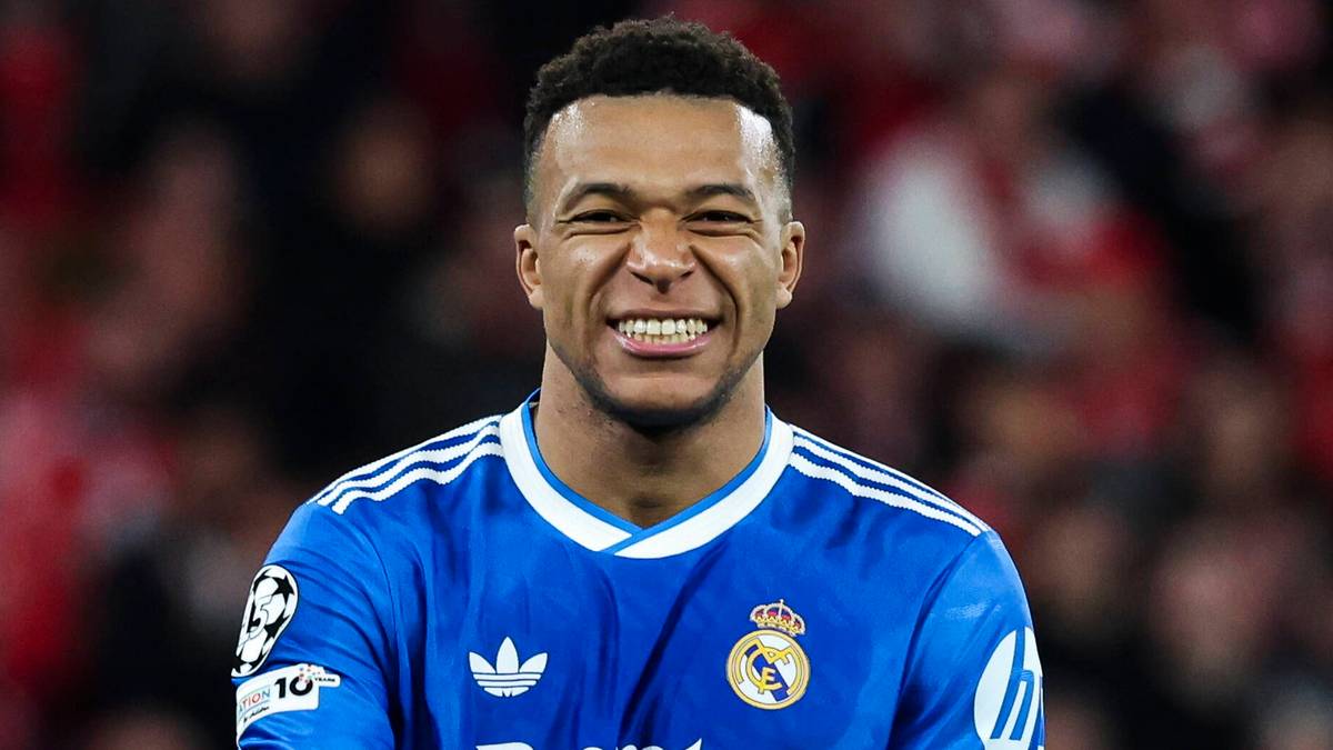 Kylian Mbappe w niebieskiej koszulce Realu Madryt uśmiecha się do kamery