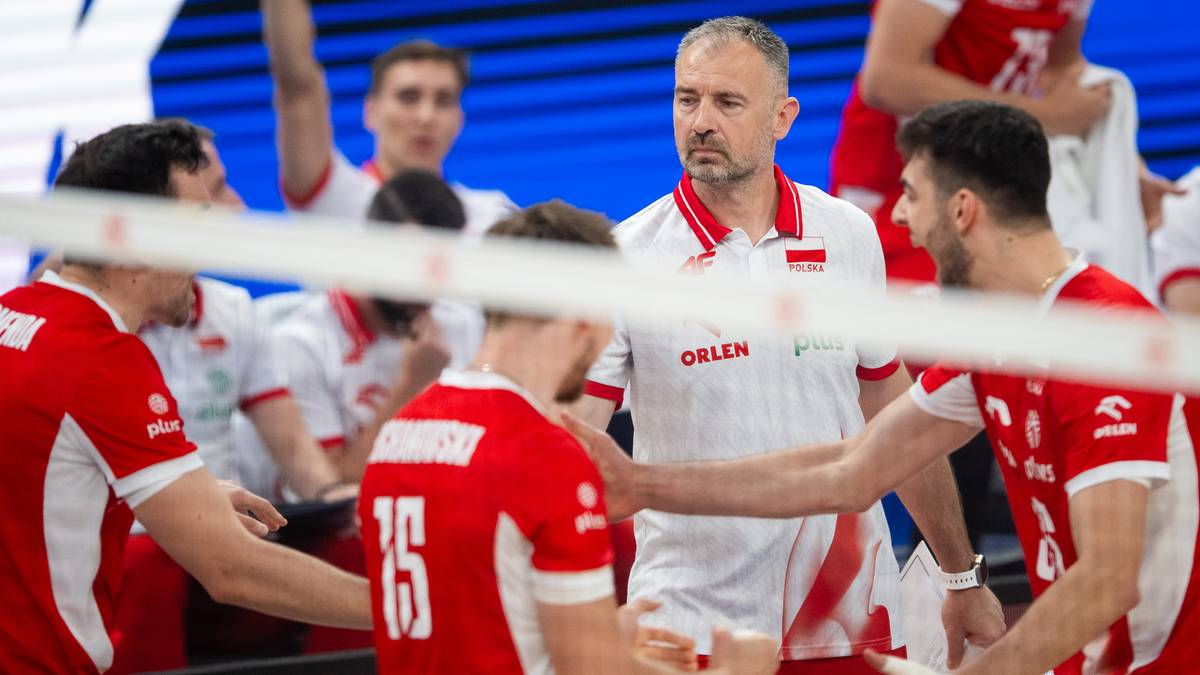 Grupa siatkarzy w czerwonych strojach reprezentacji Polski, w centrum stoi trener w białej koszulce z czerwonym kołnierzykiem.