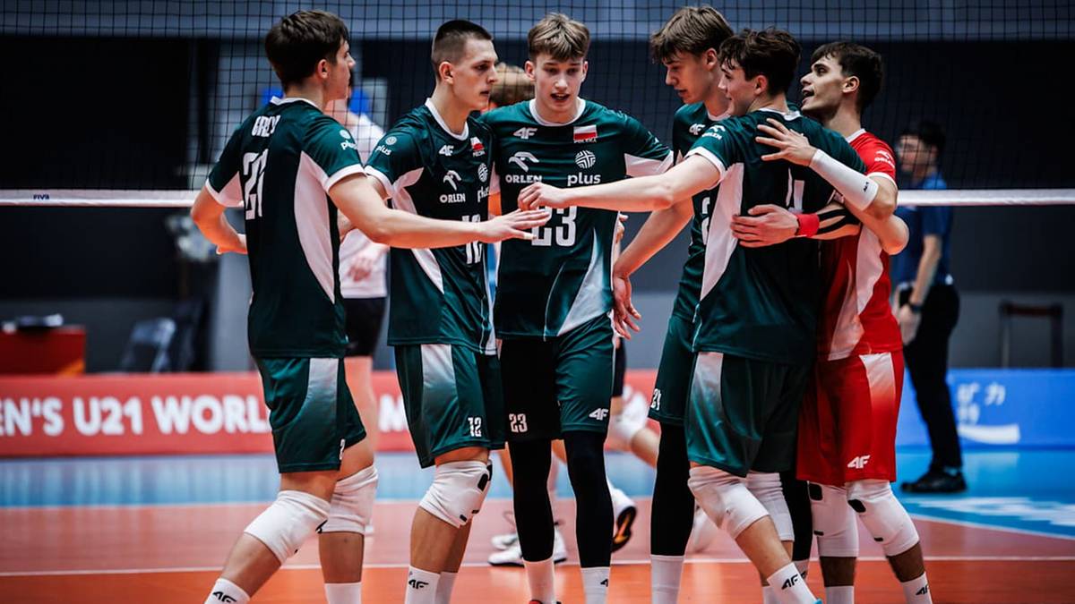 Grupa młodych polskich siatkarzy w ciemnozielonych strojach z białymi elementami, ubrani w koszulki z napisem "Polska" i numerami, przybijają sobie piątki i gratulują sobie nawzajem. W tle widać siatkę do gry i widzów.