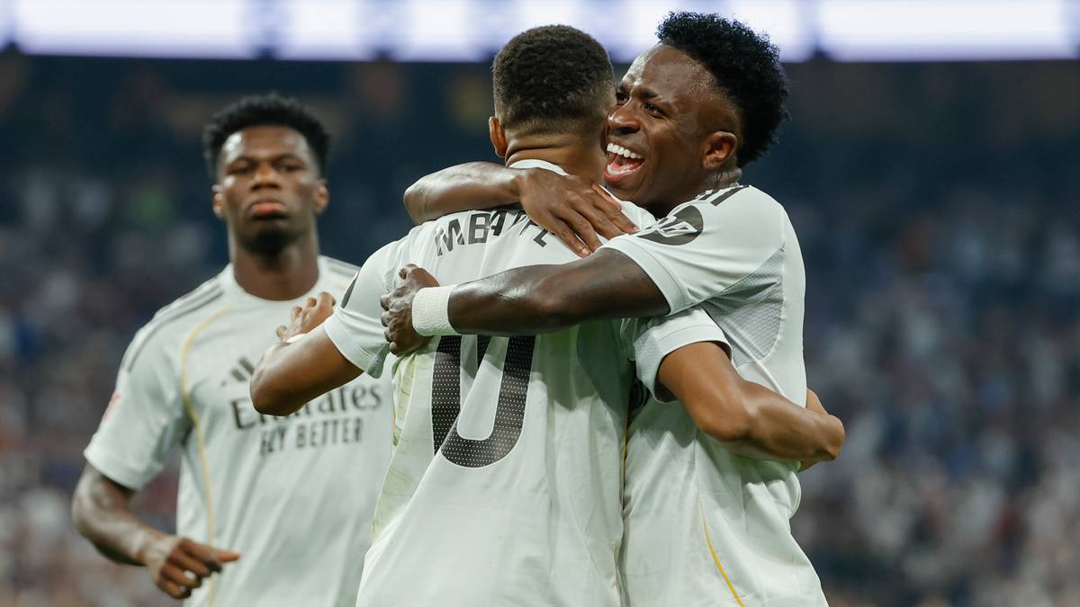 Trzej piłkarze Realu Madryt w białych koszulkach przytulają się podczas celebracji gola na boisku piłkarskim.