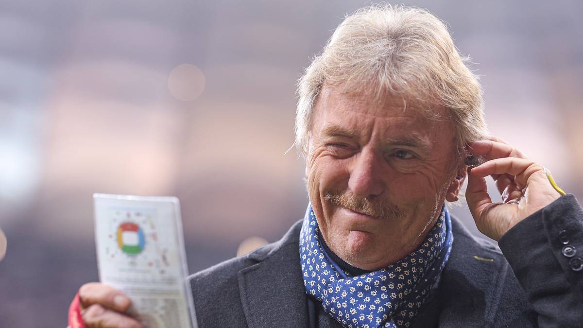 Zbigniew Boniek z siwymi włosami i wąsami trzyma w ręce dokument, na którego okładce widnieje logo z trzema kółkami w kolorach polskiej flagi.