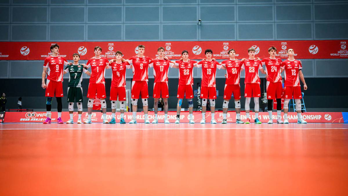 Drużyna siatkarzy reprezentacji Polski w czerwonych strojach stoi w rzędzie na hali sportowej.