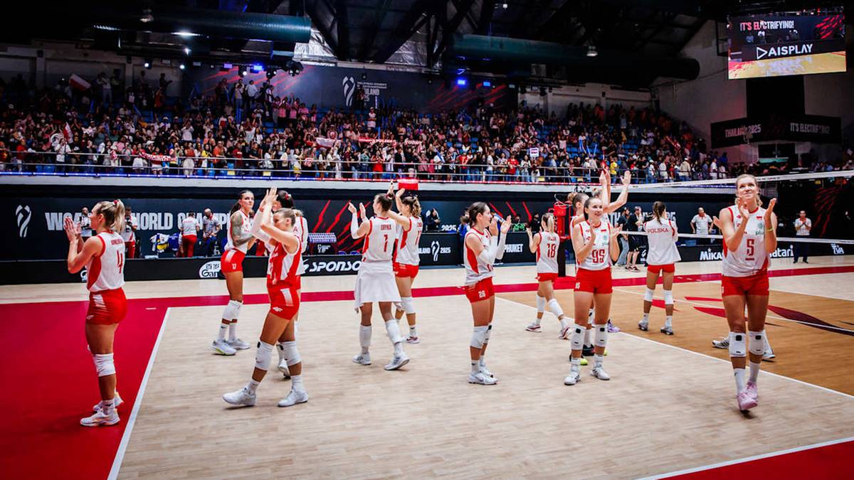 Grupa siatkarek w czerwonych strojach sportowych kłania się i klaszcze przed widownią na hali sportowej.