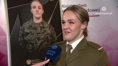 Agata Kaczmarska w mundurze wojskowym, stojąca przed plakatem ze swoim zdjęciem w wojskowym stroju.