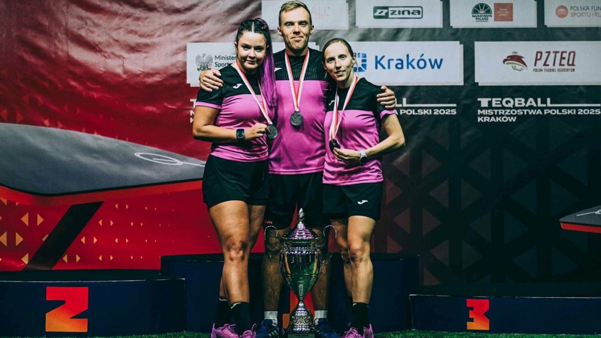 Trzech zawodników teqballa, dwie kobiety i jeden mężczyzna, pozuje do zdjęcia na podium z pucharem.
