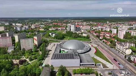 Widok z lotu ptaka na halę widowiskową z kopulastym dachem, otoczoną zabudową miejską i terenami zielonymi.