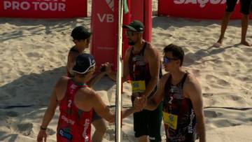 Dwóch siatkarzy plażowych wita się przy siatce po zakończonym meczu.