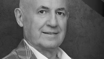 Portret starszego mężczyzny w garniturze i białej koszuli, patrzącego w obiektyw.