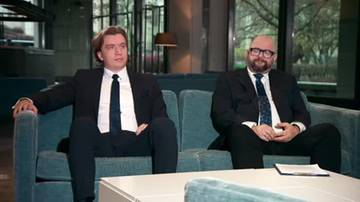 Dw&oacute;ch mężczyzn w garniturach siedzi na kanapie.