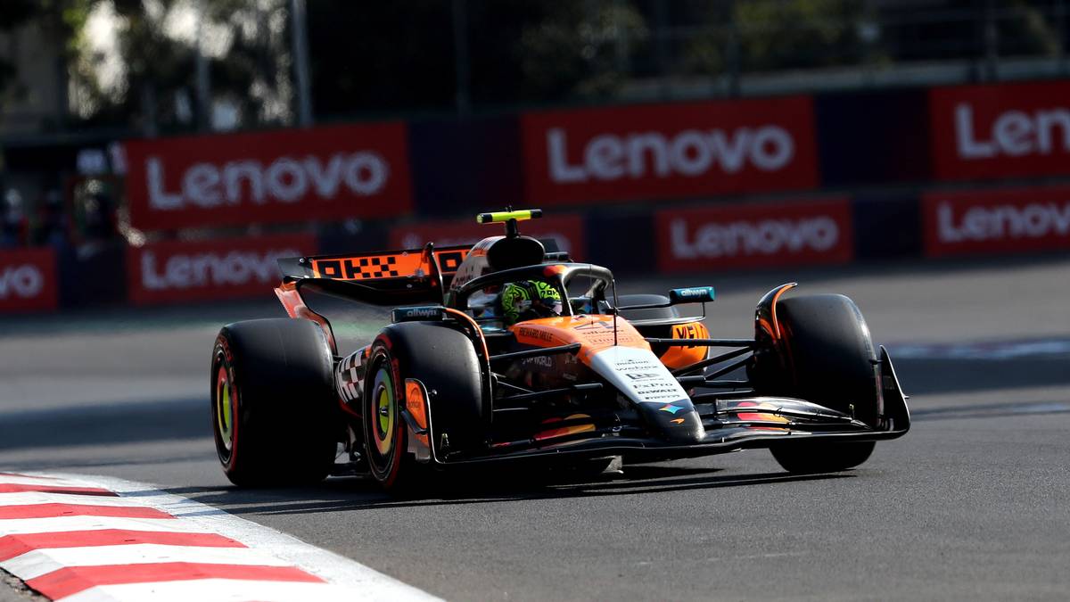 Bolid Formuły 1 w barwach pomarańczowo-czarnych jedzie po torze.