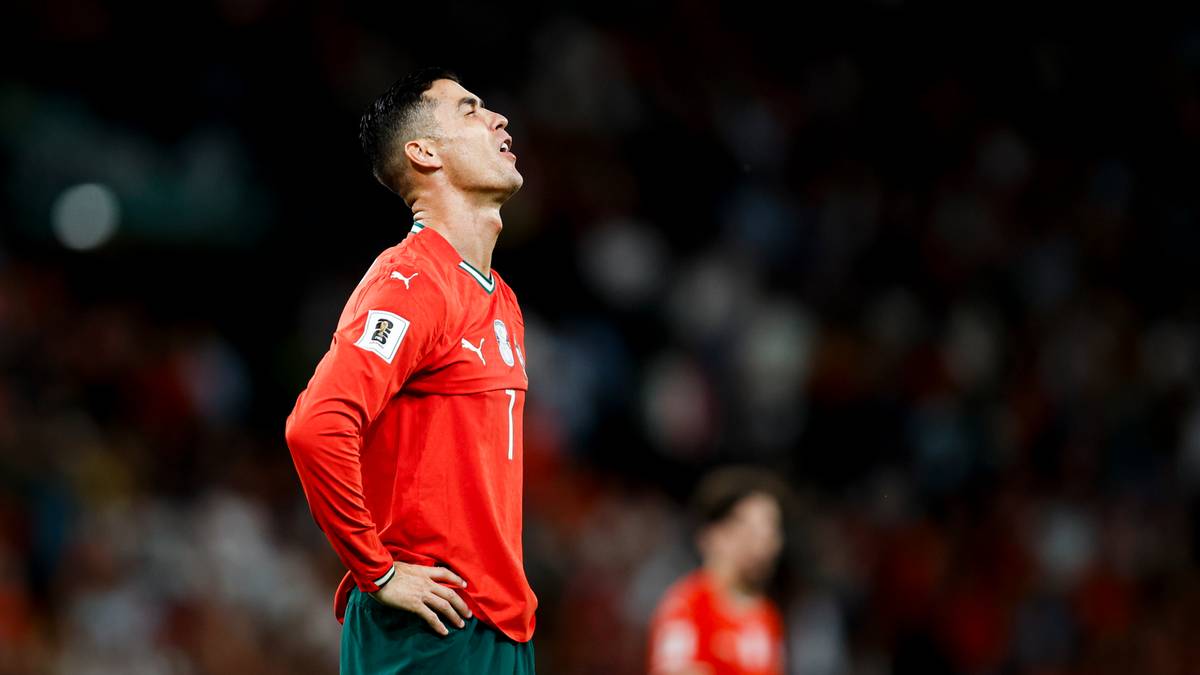 Piłkarz w czerwonej koszulce patrzy w górę z wyrazem rozczarowania na twarzy podczas meczu.