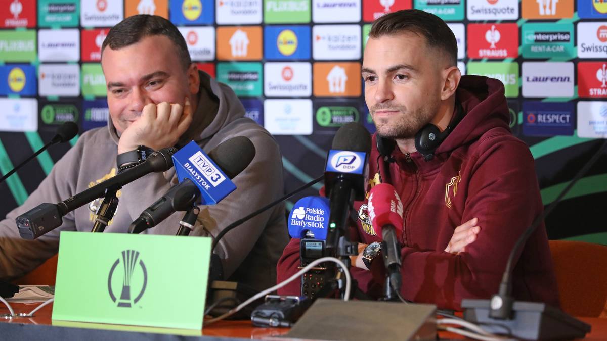 Dw&oacute;ch mężczyzn siedzi przy stole z mikrofonami, podczas gdy jeden opiera głowę na dłoni, a drugi patrzy prosto przed siebie.