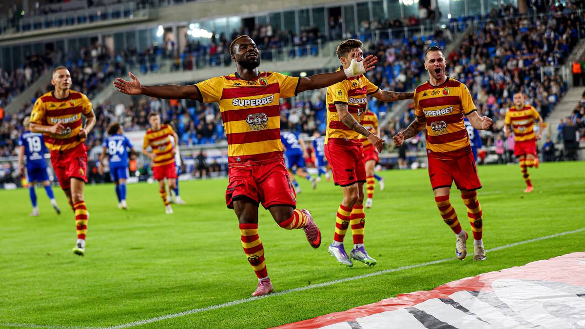 Piłkarze Jagiellonii Białystok w czerwono-złotych strojach cieszą się z gola, na pierwszym planie jeden z zawodnik&oacute;w biegnie z rękami otwartymi.