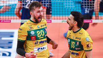 Dw&oacute;ch siatkarzy w ż&oacute;łtych koszulkach z zielonymi akcentami radośnie krzyczy do siebie na tle siatki.