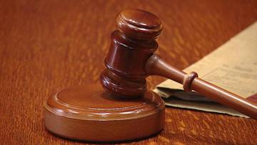 Drewniany młotek sędziowski i jego podstawa na tle dokumentów.