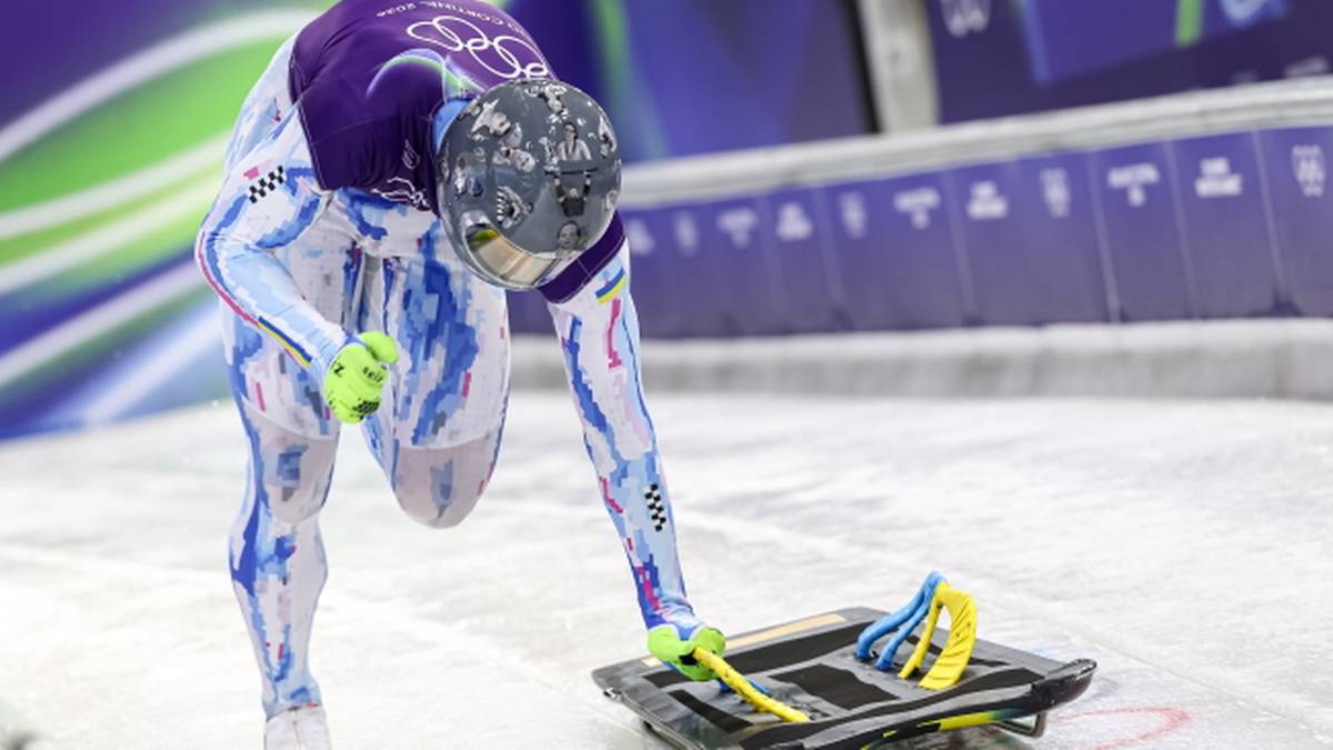 Skeletonista w kasku z wizerunkami poległych ukraińskich sportowc&oacute;w na lodowym torze, pochylony nad swoim skeletonem.