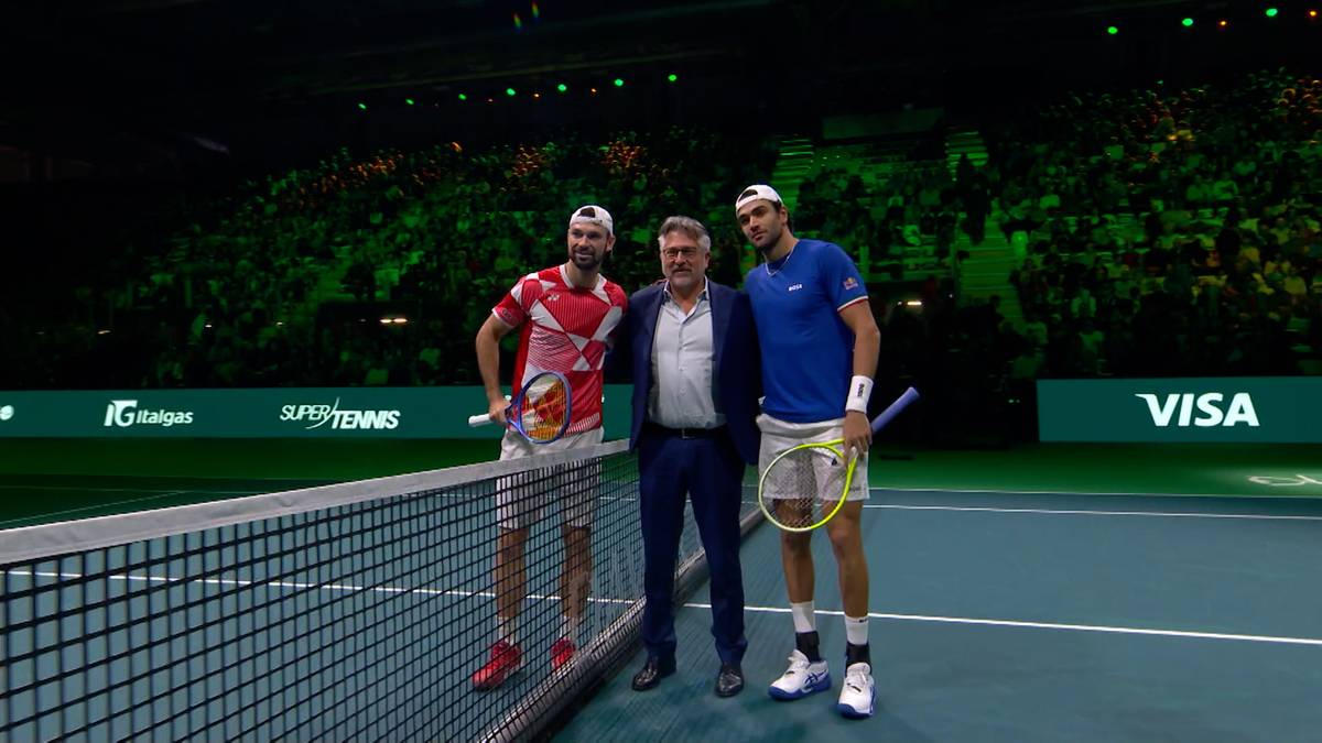 Dwóch tenisistów i mężczyzna w garniturze stoją na korcie tenisowym.