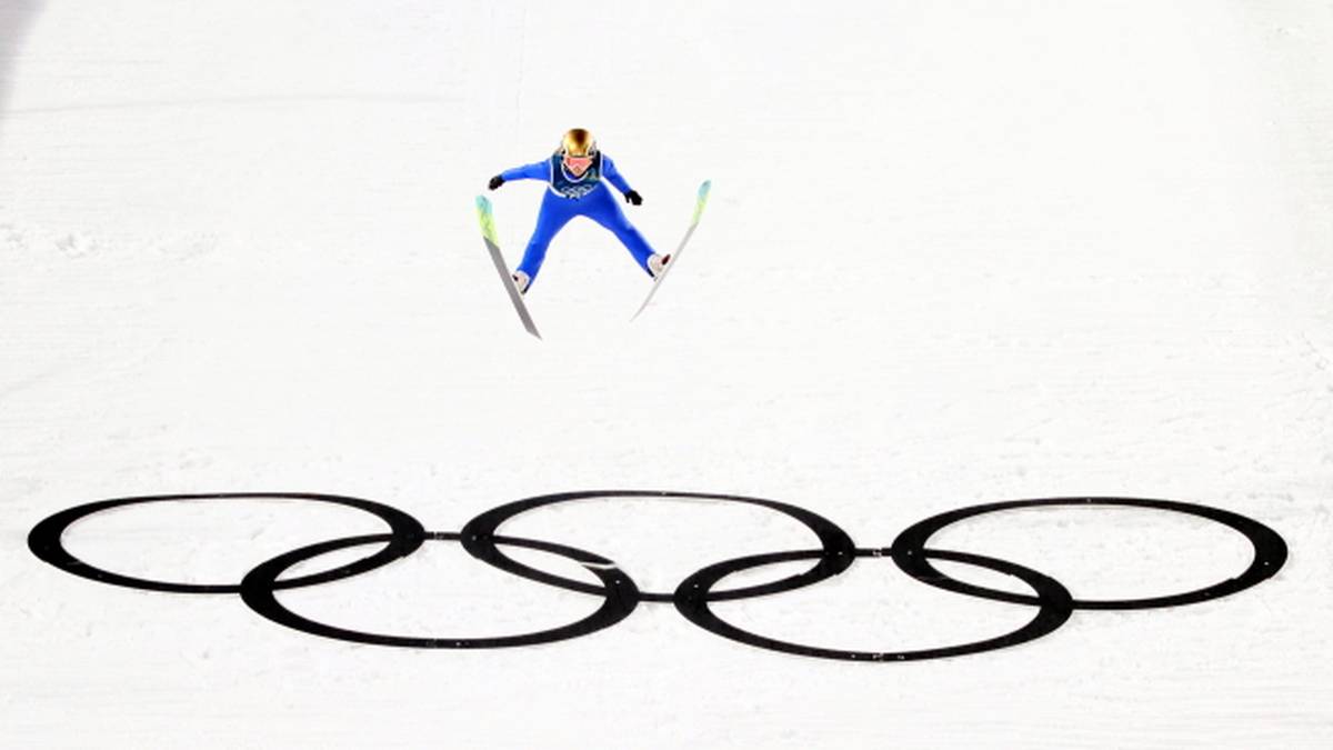 Skoczek narciarski w powietrzu nad logo igrzysk olimpijskich