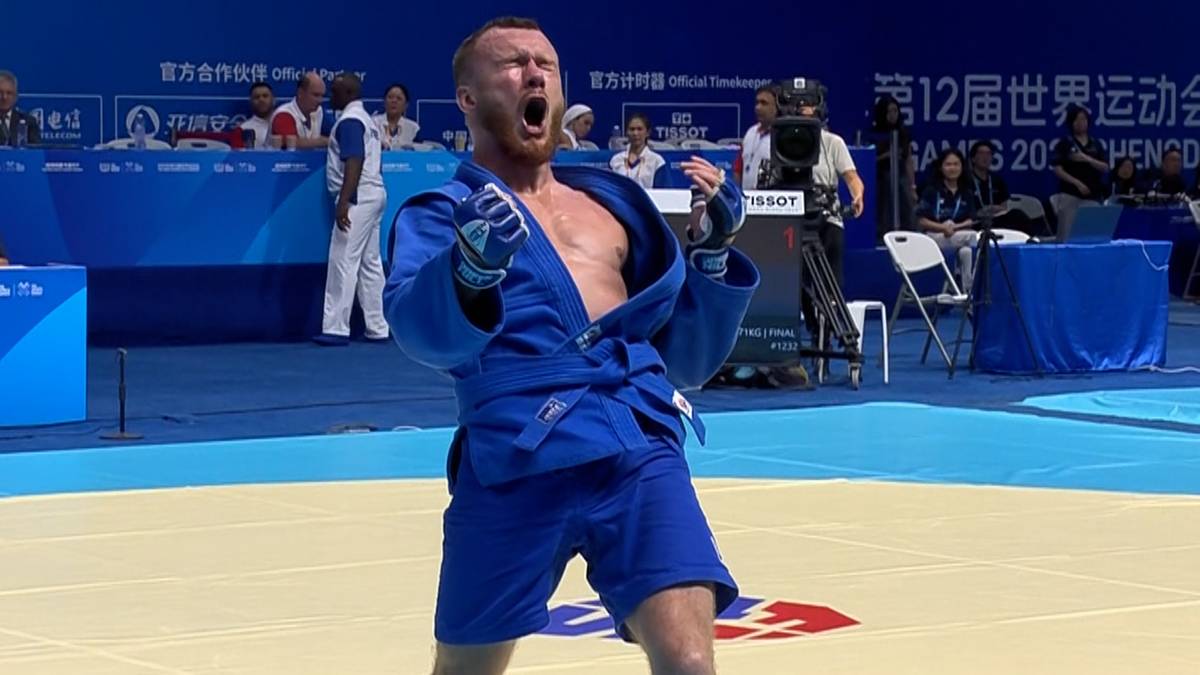 Zawodnik sambo w niebieskim stroju, z zaciśniętymi pięściami i otwartymi ustami, wyraża radość po wygranej walce.