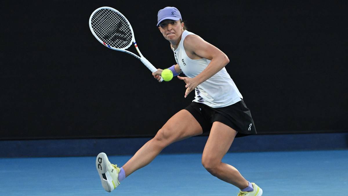 Iga Świątek w akcji na korcie tenisowym, z rakietą w dłoni i gotowością do odbicia piłki.