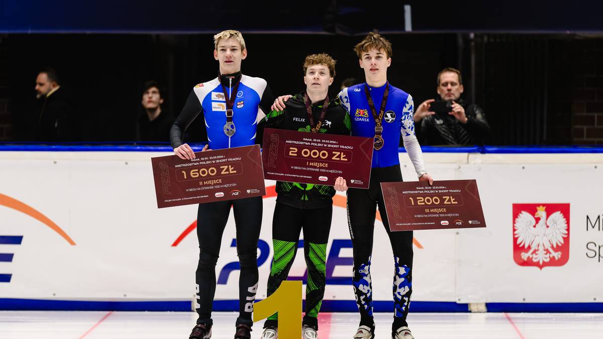 Trzej młodzi mężczyźni na podium w strojach sportowych, trzymający tabliczki z nagrodami pieniężnymi i medalami.