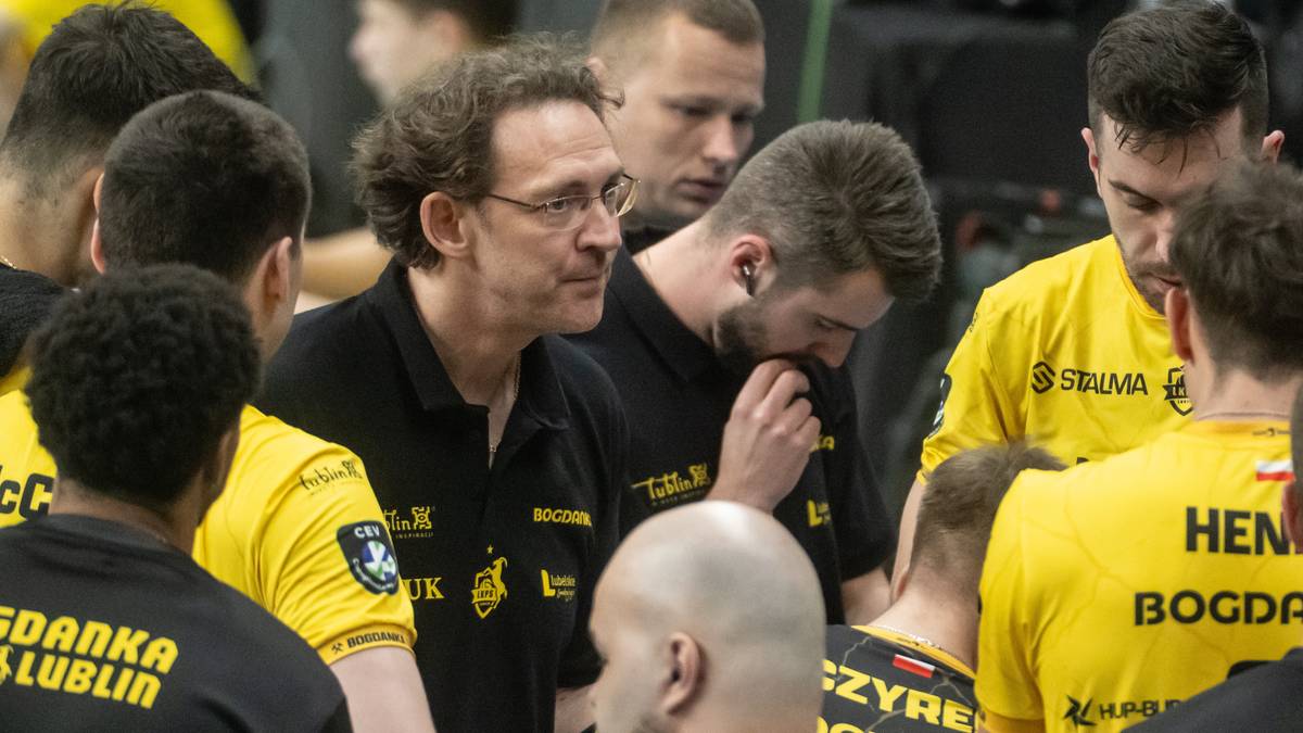 Trener w okularach rozmawia z grupą siatkarzy w czarnych i ż&oacute;łtych strojach.